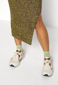 Gonna verde a coste con uno spacco laterale abbinata a sneakers bianche con accenti marroni e calze a coste verde chiaro.