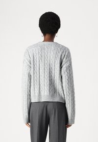 Pull gris en maille torsadée avec ourlet côtelé et encolure ronde. Le tissu semble doux, avec un motif texturé et en relief sur la surface.