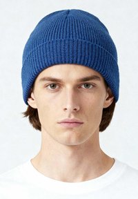 Blauwe geribde gebreide muts met een afgeronde bovenkant en dik, textuurrijk materiaal. Wordt gedragen met de rand naar beneden getrokken om de oren te bedekken. Heeft een eenvoudig, minimalistisch ontwerp.