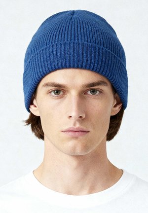 Blauwe geribde gebreide muts met een afgeronde bovenkant en dik, textuurrijk materiaal. Wordt gedragen met de rand naar beneden getrokken om de oren te bedekken. Heeft een eenvoudig, minimalistisch ontwerp.