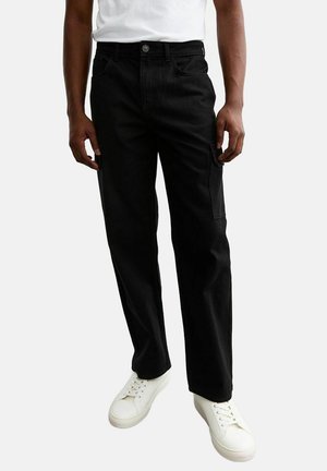Black cargo pants made of sturdy cotton with a straight leg design, featuring side pockets and a button closure. Worn with white sneakers.