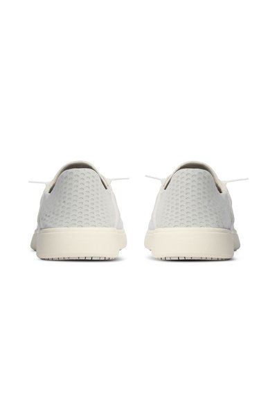 Par de zapatillas bajas blancas con textura de punto y suelas blancas mostradas por detrás sobre un fondo blanco.