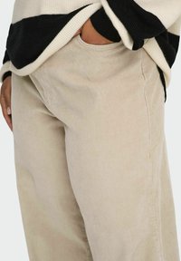 Bež široke hlače od korduroga s diskretnim okomito rebrastim uzorkom, s bočnim džepom i klasičnim, opuštenim krojem.