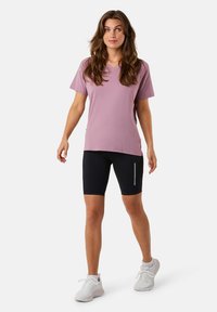 Lichtpaarse v-hals t-shirt met korte mouwen, gecombineerd met zwarte fietsbroeken met een reflecterende strook. Witte sportschoenen.