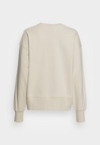 Kremfärgad långärmad sweatshirt med ribbstickade muddar och fåll, visad bakifrån mot en enfärgad vit bakgrund.