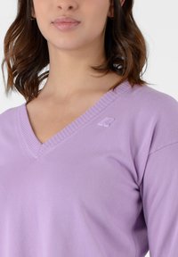Maglione lavanda a scollo a V realizzato in morbido tessuto a maglia, con bordi a coste e un piccolo logo sul lato sinistro del petto.