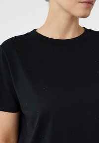 Close-up of a person wearing a black T-shirt with small, shiny embellishments scattered across the fabric.