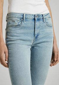Jeans de mezclilla azul claro con un diseño ajustado, que cuentan con bolsillos frontales, un cierre de botón y un ligero desvanecimiento a lo largo de los muslos.