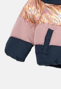 Puffjakke med erme i tre fargeblokker: skinnende iriserende rosegull, matt støvete rosa og matt mørk marineblå.