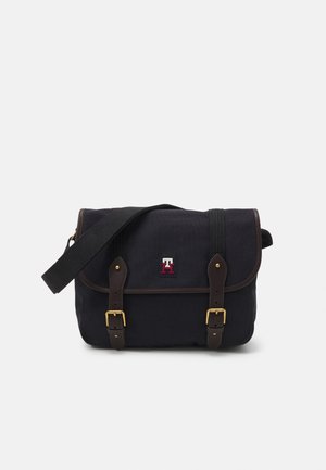 Borsa a tracolla in tessuto nero con cinturini in pelle marrone scuro, fibbie dorate, tracolla regolabile e piccolo logo ricamato rosso e bianco.