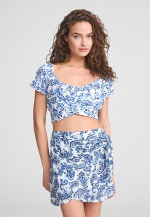 Top corto azzurro chiaro con maniche a volant e stampa paisley, abbinato a una gonna avvolgente coordinata che presenta un design simile e un dettaglio con fiocco.