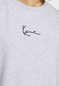 Grijs katoenen T-shirt met een zwart geborduurde handtekening op de borst. Rond halsontwerp met een gestructureerde, licht gemêleerde stof.