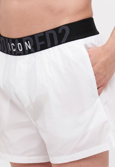 Shorts blancs en tissu léger, dotés d'une taille élastique noire avec l'inscription grise "ICON" et de poches latérales.