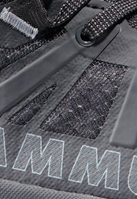 Svart idrottssko i närbild har en övre del i mesh med utskurna detaljer, textil med struktur och en blå accentlogga på sidan.