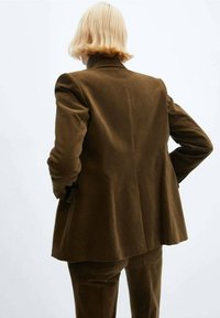 Brązowa marynarka z sztruksu o luźnym kroju, z wyciętym kołnierzem i podkreślonymi ramionami. Widok od tyłu ukazuje czysty, minimalistyczny design.