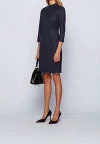 Mörkblå klänning i skärning med trekvartslånga ärmar, slät textur. Matchad med svart handväska och spetsiga klackar för en elegant look.