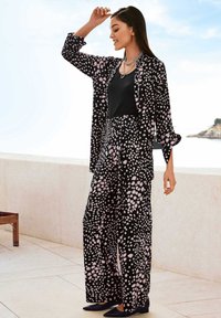 Black and pink spotted two-piece outfit featuring a loose long-sleeve shirt and wide-leg pants. Smooth fabric with a relaxed fit.