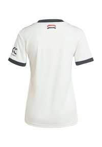 Maglietta sportiva bianca con colletto e polsini scuri; presenta un logo sulla manica sinistra e un piccolo disegno colorato sul retro del collo.