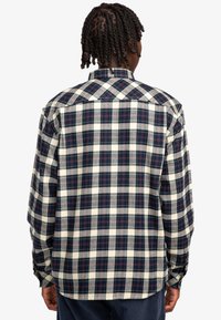 Camisa de franela a cuadros que presenta una mezcla de cuadrados en azul oscuro, blanco y burdeos; mangas largas y puños abotonados; textura suave.