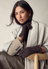 Brown suede gloves with a snug fit, worn with a light gray wrap featuring black trim and a beige coat with button details, set against a neutral background.