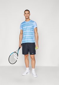 Blå og hvit stripet trenings T-skjorte, svarte shorts, hvite joggesko, holder et tennisracket og en gul tennisball.