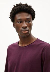 Paarse langekoushemd met een rond decolleté, met een gladde textuur en een eenvoudig ontwerp. Het model heeft kort, krullend donker haar.