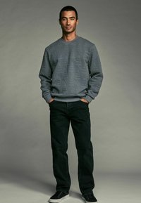 Gray sweatshirt with textured triangular pattern, relaxed fit, ribbed cuffs, paired with black jeans and black sneakers.