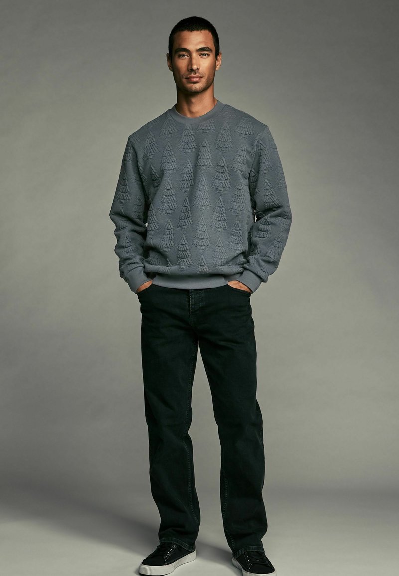 Sweatshirt gris avec un motif triangulaire texturé, coupe décontractée, poignets côtelés, associé à un jean noir et des baskets noires.