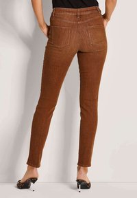 Bruine, strak aansluitende jeans met een gladde textuur, achterzakken en een middelhoge taille, gecombineerd met hoge sandalen in tijgerprint.