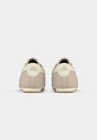 Biege Adidas sporta apavi, redzami no aizmugures uz vienkārša balta fona.