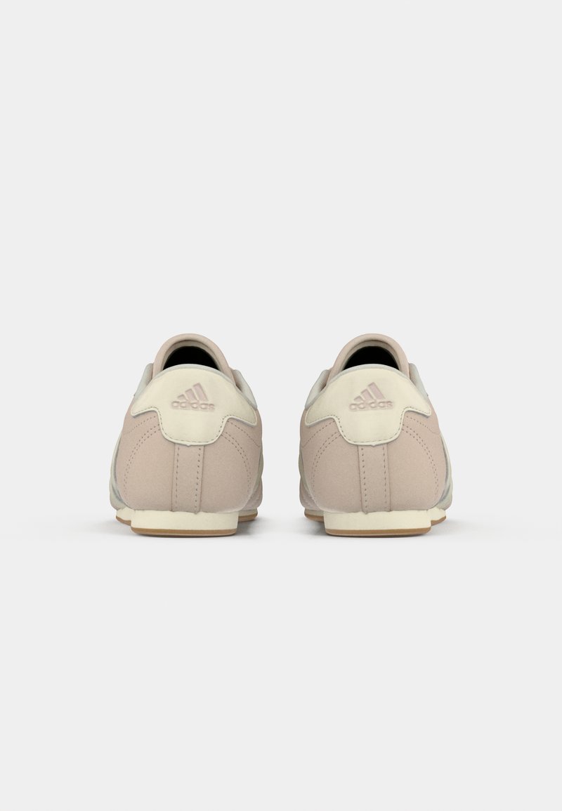 Un par de zapatillas Adidas beige vistas desde atrás sobre un fondo blanco liso.