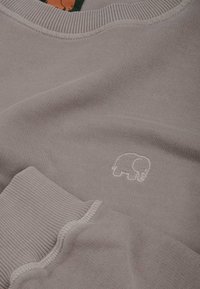 Sudadera gris claro con cuello y puños acanalados. Presenta un pequeño logo de elefante blanco en el pecho. Textura de tela suave.
