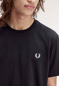 Zwarte katoen t-shirt met een ronde halslijn. Bevat een klein wit geborduurd lauriert logo op de linkerborst. Gladde textuur.