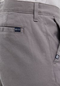 Shorts tissés gris avec une finition texturée, dotés d'une poche latérale et d'une étiquette de marque bleu marine avec un logo en forme d'étoile blanche.