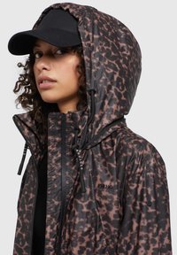 Giacca impermeabile con stampa animale marrone e nera, dotata di cappuccio regolabile, chiusura con zip e branding discreto sul petto.