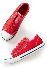 Red canvas sneakers with white rubber toe cap and sole. Features black stripe along the sole and red lace eyelets. Brand label visible.