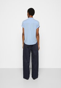 Blouse bleu clair à manches courtes avec un pli dans le dos, associée à un pantalon large bleu marine, offrant une texture lisse et une coupe décontractée.