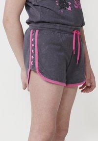 Shorts grigi con cordoncino e rifiniture rosa, decorati con motivi a stella sui lati. Il tessuto sembra morbido e dal design informale.