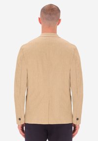 Blazer beige, strutturato con una vestibilità su misura, due bottoni ai polsini e una fessura singola sul retro. Tessuto liscio con un motivo sottile.