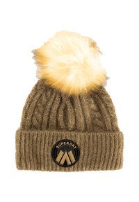 Berretto lavorato a maglia color beige con risvolto, dotato di un soffice pom-pom biondo sulla parte superiore e di una patch rotonda nera con la scritta "SUPERDRY".