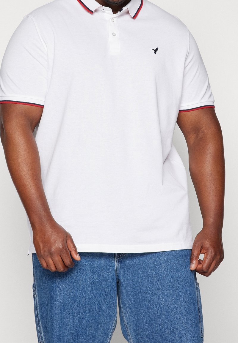 Biała koszulka polo z kołnierzykiem w czerwono-granatowe paski, krótkimi rękawami z kontrastową lamówką oraz małym czarnym logo na piersi.