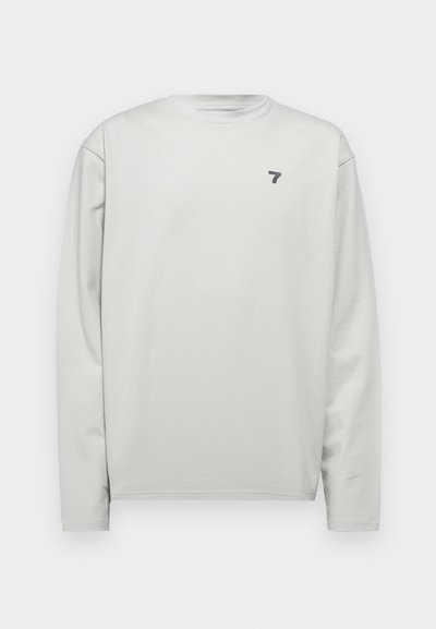 Light gray long-sleeve shirt with a round neck, featuring a textured fabric and a small navy logo on the left chest.