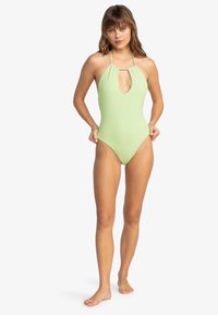Maillot de bain une pièce vert clair à côtes, avec un col halter, une découpe en forme de clé et des emmanchures hautes pour une silhouette élégante.