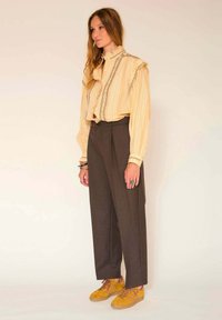 Blouse jaune pâle avec des rayures verticales et un col volanté, associée à un pantalon marron taille haute et des baskets en suède jaunes.