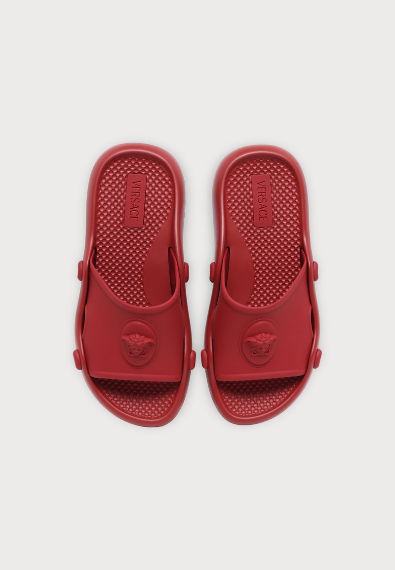 Paar rote Gummi-Sandalen mit strukturiertem Fußbett und Medusa-Kopf-Emblem auf den oberen Riemen, von oben gesehen.
