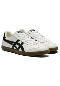 Scarpe sportive bianche in pelle con accenti neri, caratterizzate da una finitura texturizzata, punta rotonda, linguetta imbottita e suola in gomma.
