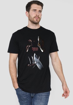 Man wearing black t-shirt with "Freddy vs Jason" text and graphic of Freddy Krueger’s claws and Jason’s mask, standing against plain background.