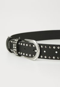 Ceinture en cuir noir avec des clous métalliques argentés et une boucle argentée. Texture lisse avec un design classique et plusieurs perforations.