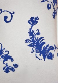 Tessuto bianco con intricate fantasie floreali e a spirale blu, caratterizzato da una texture liscia e un design lavorato a maglia dettagliato in tutta la superficie.