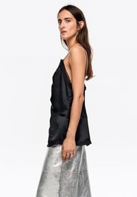 Czarna satynowa koszulka na ramiączkach z koronkowymi zdobieniami, cienkimi paskami i luźnym krojem, zestawiona z metaliczną srebrną spódnicą. Gładka faktura na całej powierzchni.